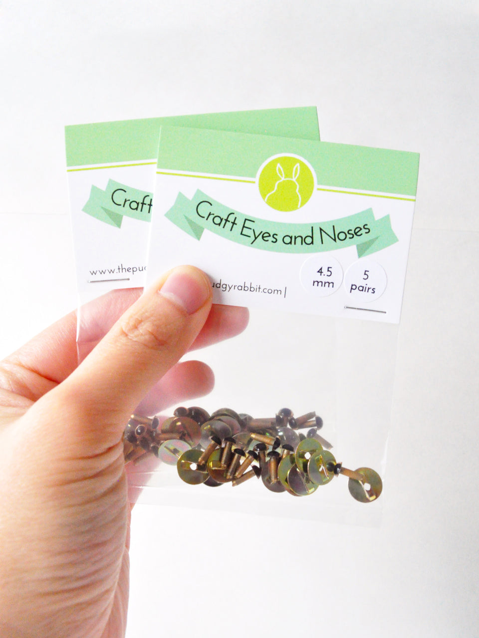 Hand holding packages of gold craft eyes with a white background