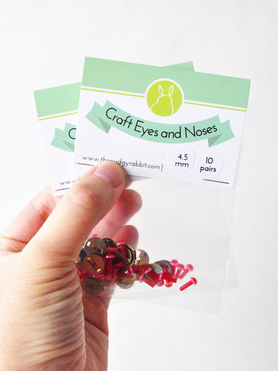 Hand holding packs of pink and red craft eyes in front of a white background.