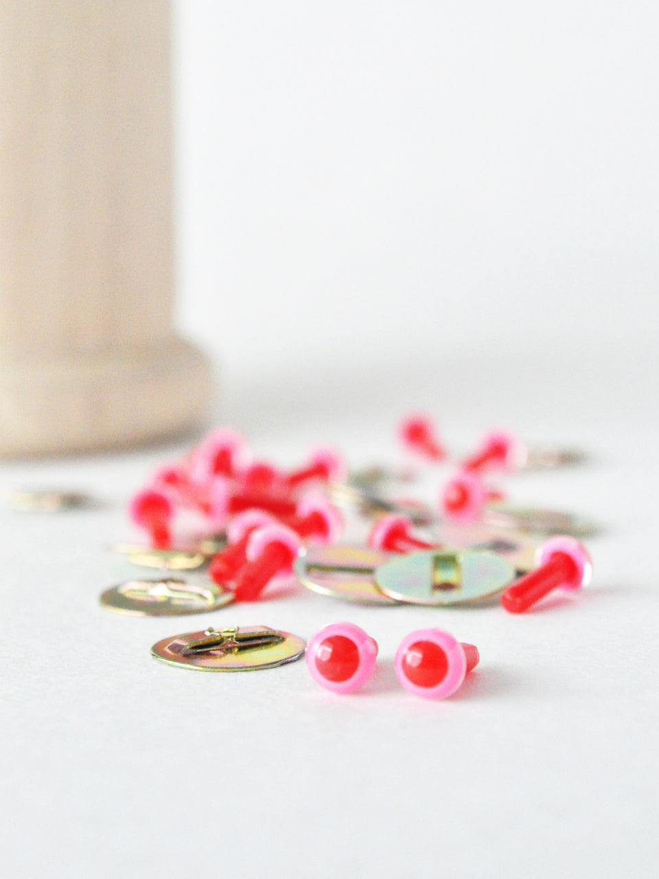 pink and red safety eyes with metal washers on a white surface.