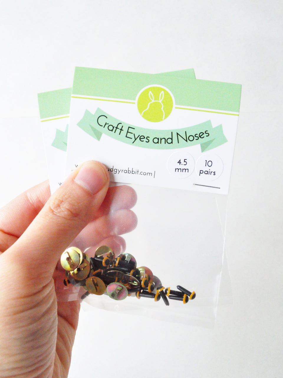 Hand holding packages of yellow craft eyes on a white background.