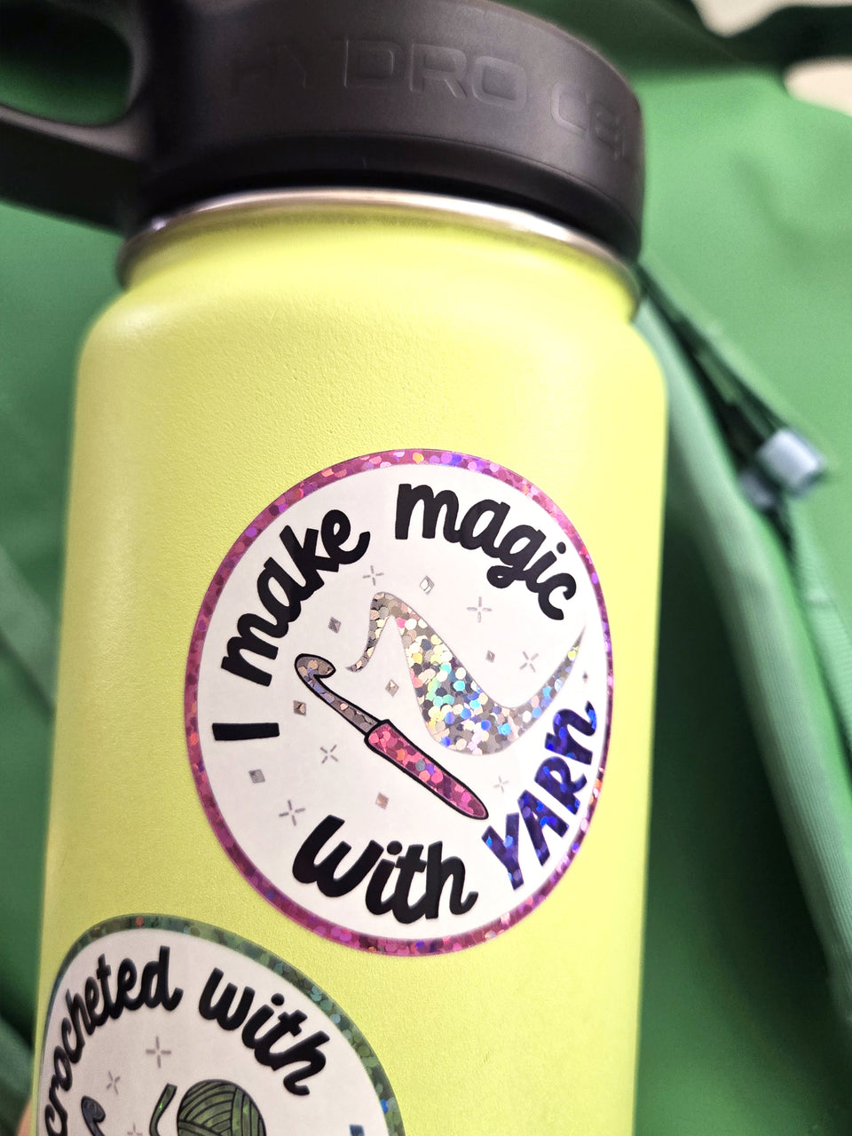 Glittery sticker that says "I make magic with yarn" applied on a green water bottle.