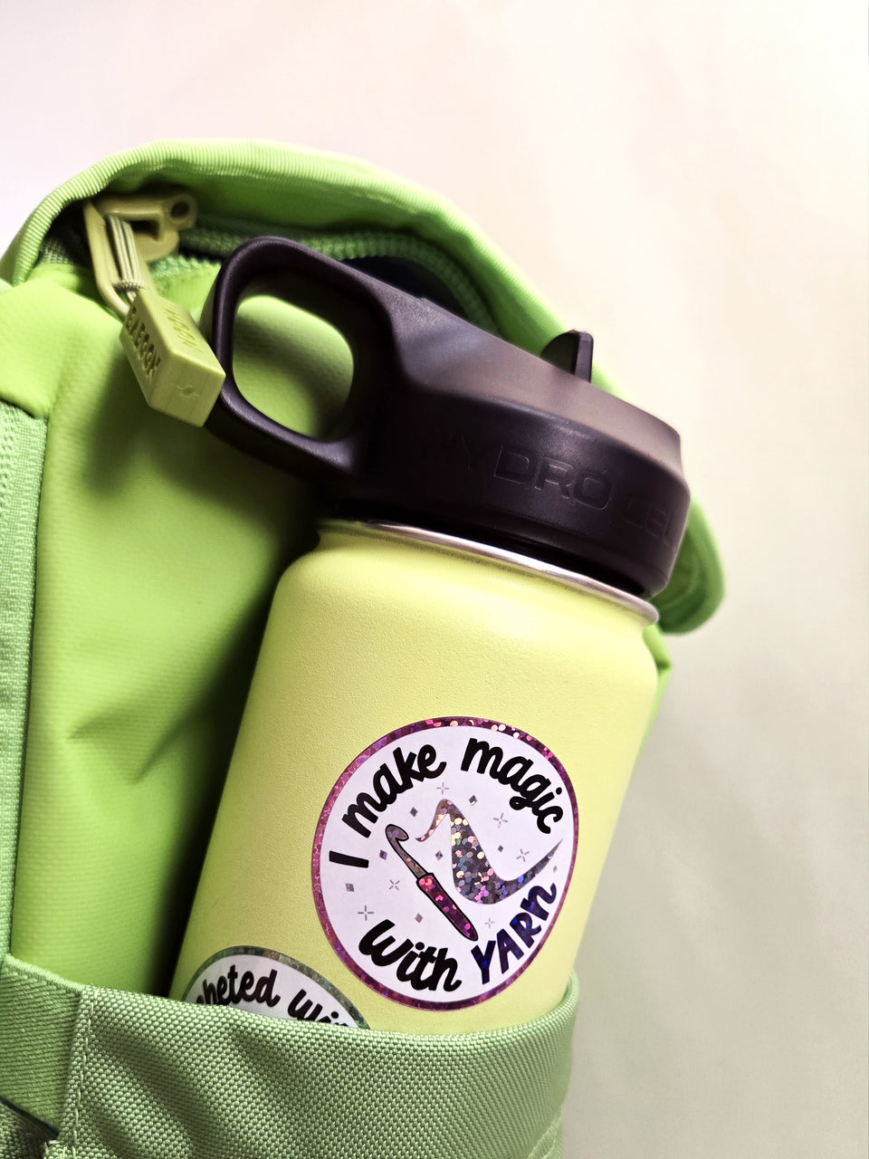 "I make magic with yarn" crochet sticker applied on a green water bottle in the side pocket of a green backpack.