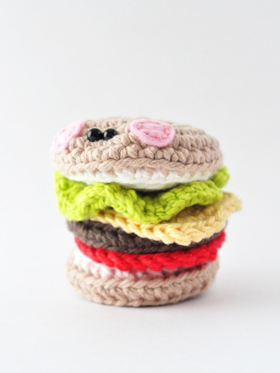 Crocheted hamburger with pink cheeks on white background, crochet pattern by The Pudgy Rabbit