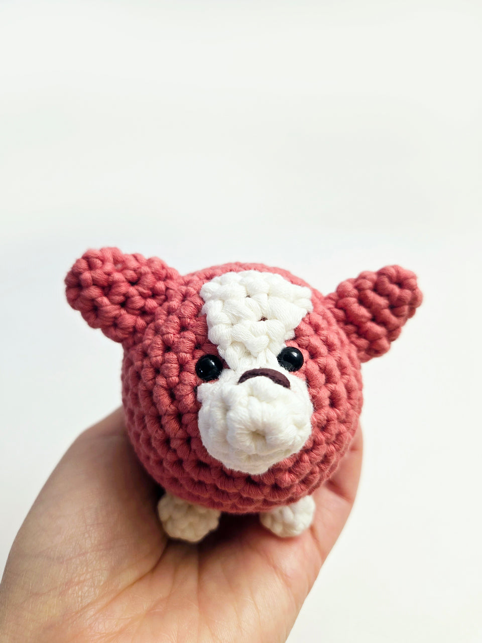 Red and white corgi amigurumi in the palm of a hand.