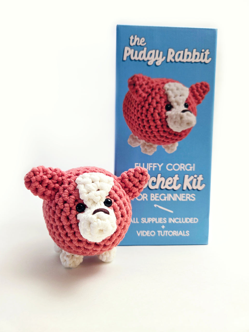 Red and white crochet corgi in front of a DIY corgi crochet kit by The Pudgy Rabbit.