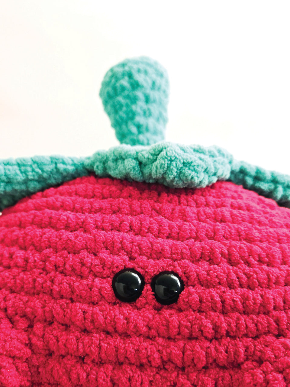Close-up of a crocheted strawberry with a green leaf on a white background