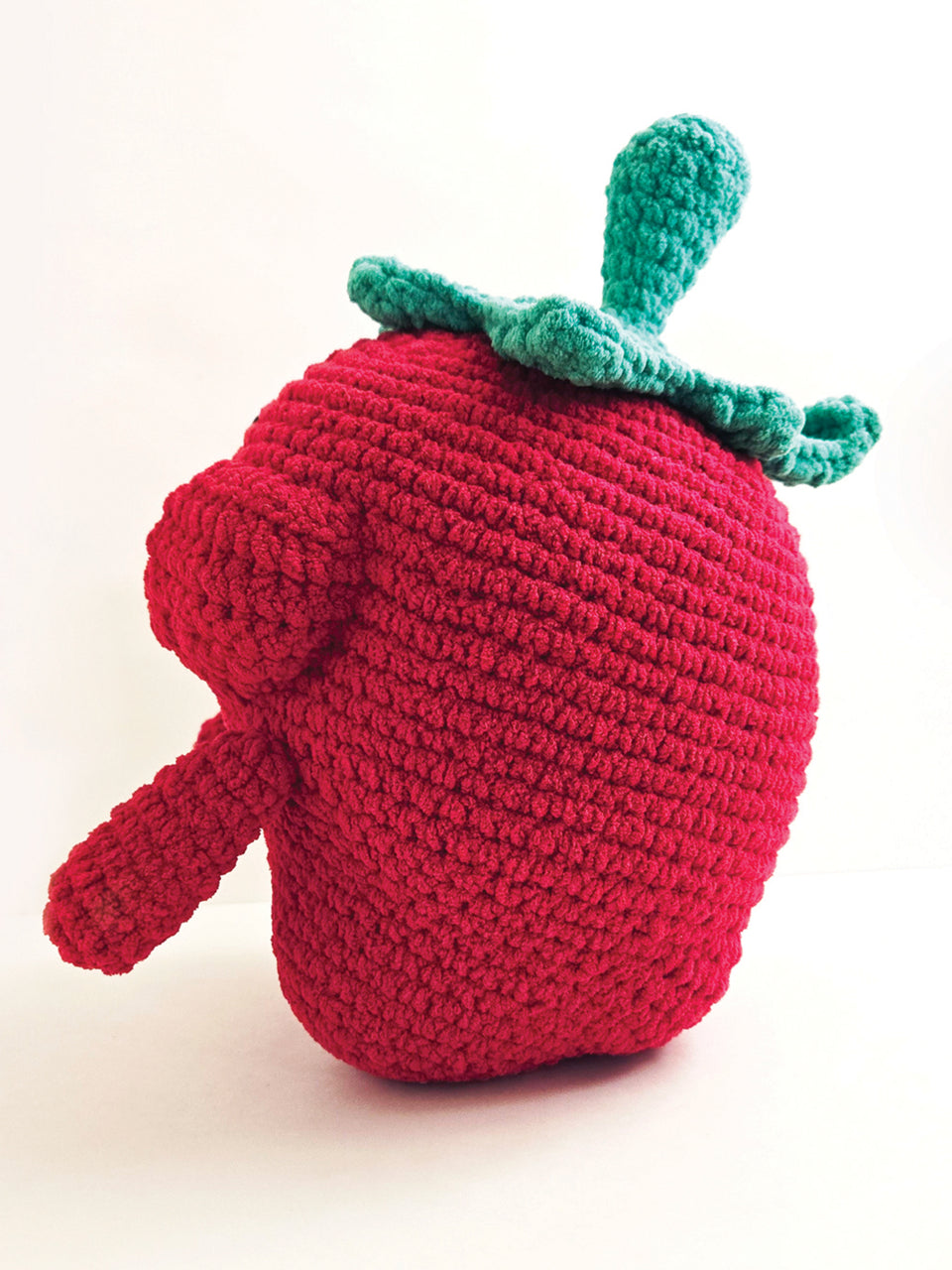 Crocheted strawberry toy with a green leaf on a white background
