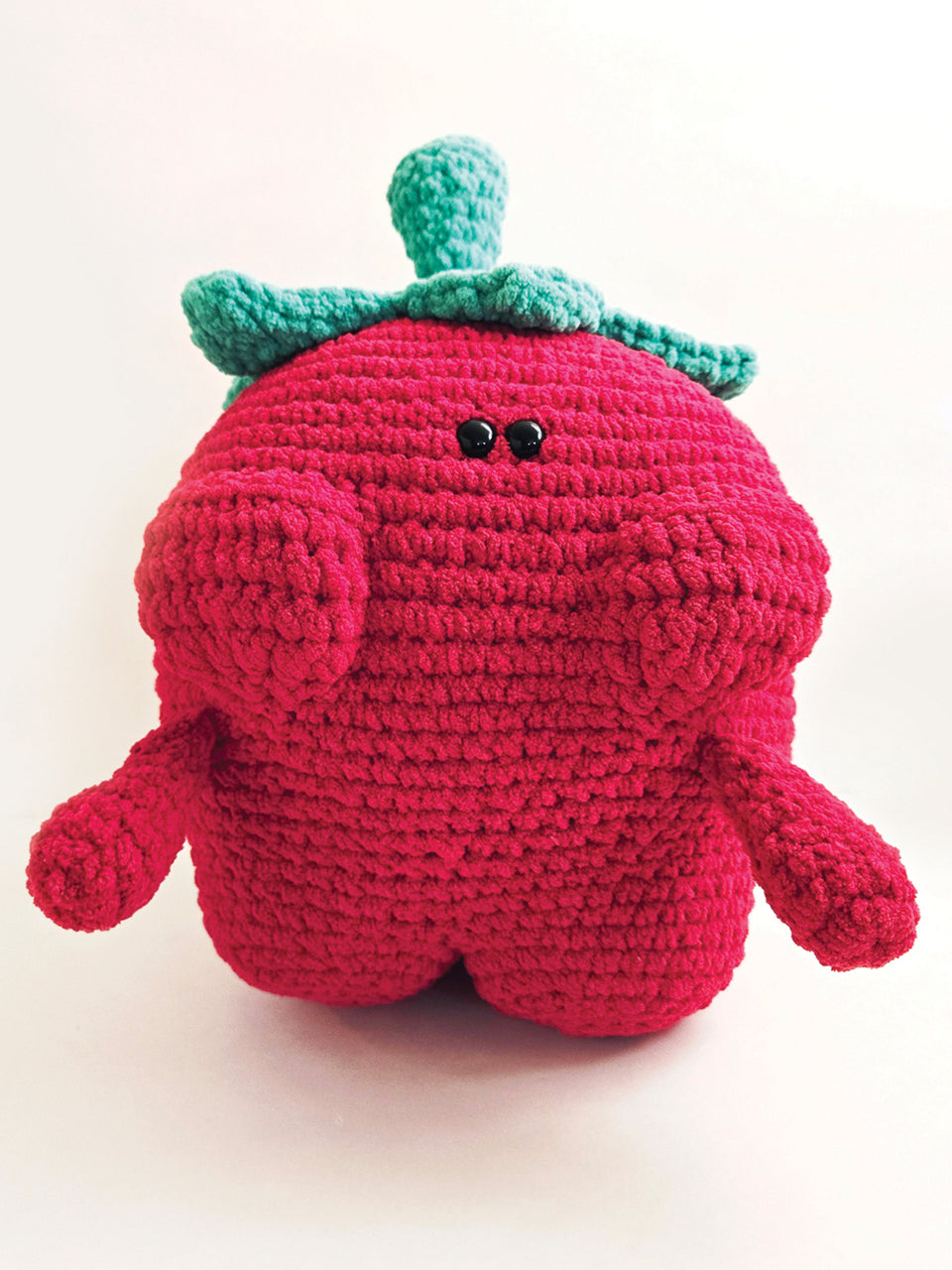 Crocheted strawberry plush toy with green leaves on a white background