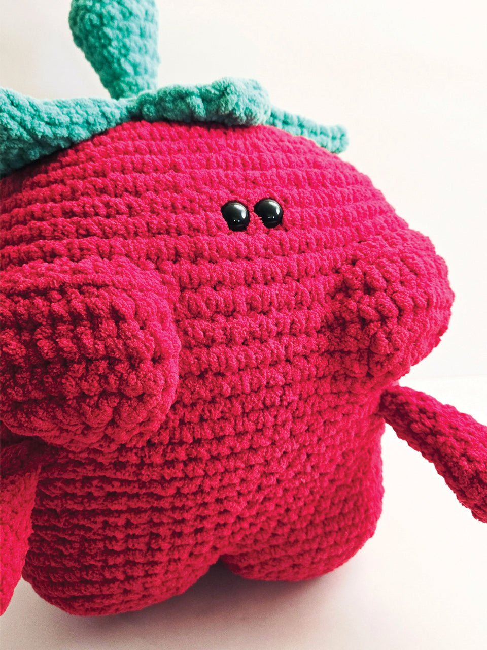 Crocheted strawberry with a green hat on a light background