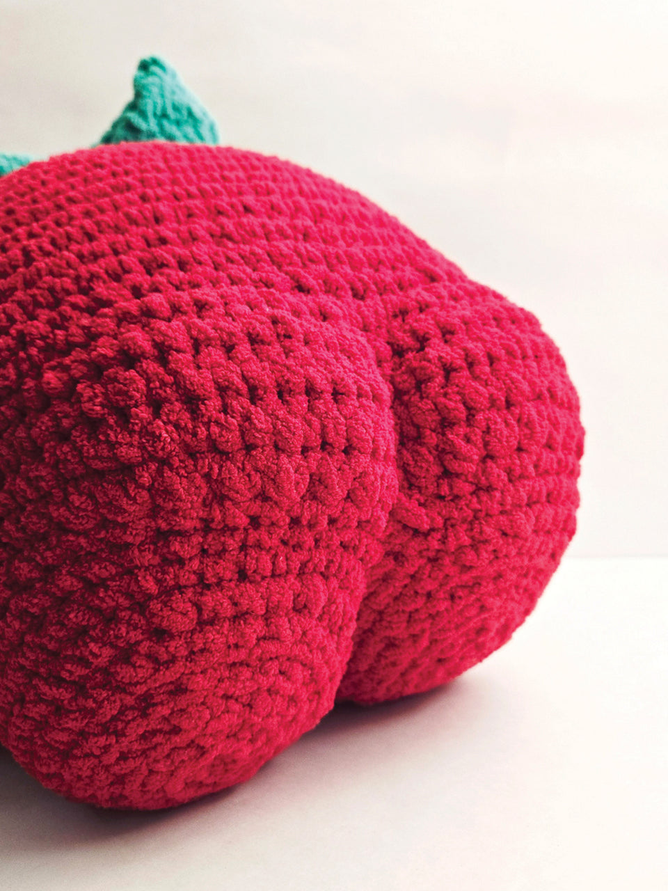 Crocheted strawberry butt with a green stem on a white background