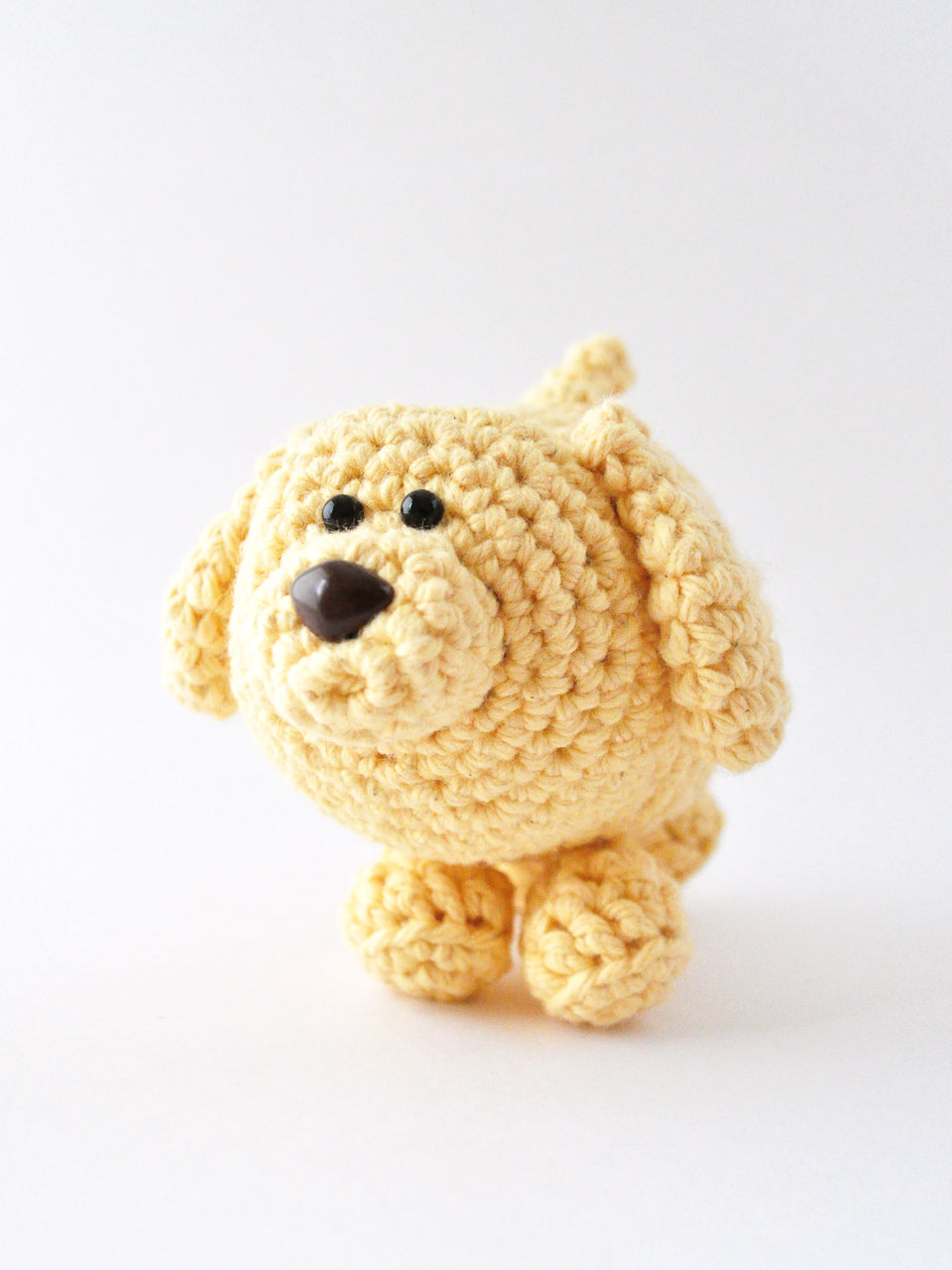 Crocheted yellow dog on a white background, amigurumi pattern by The Pudgy Rabbit.