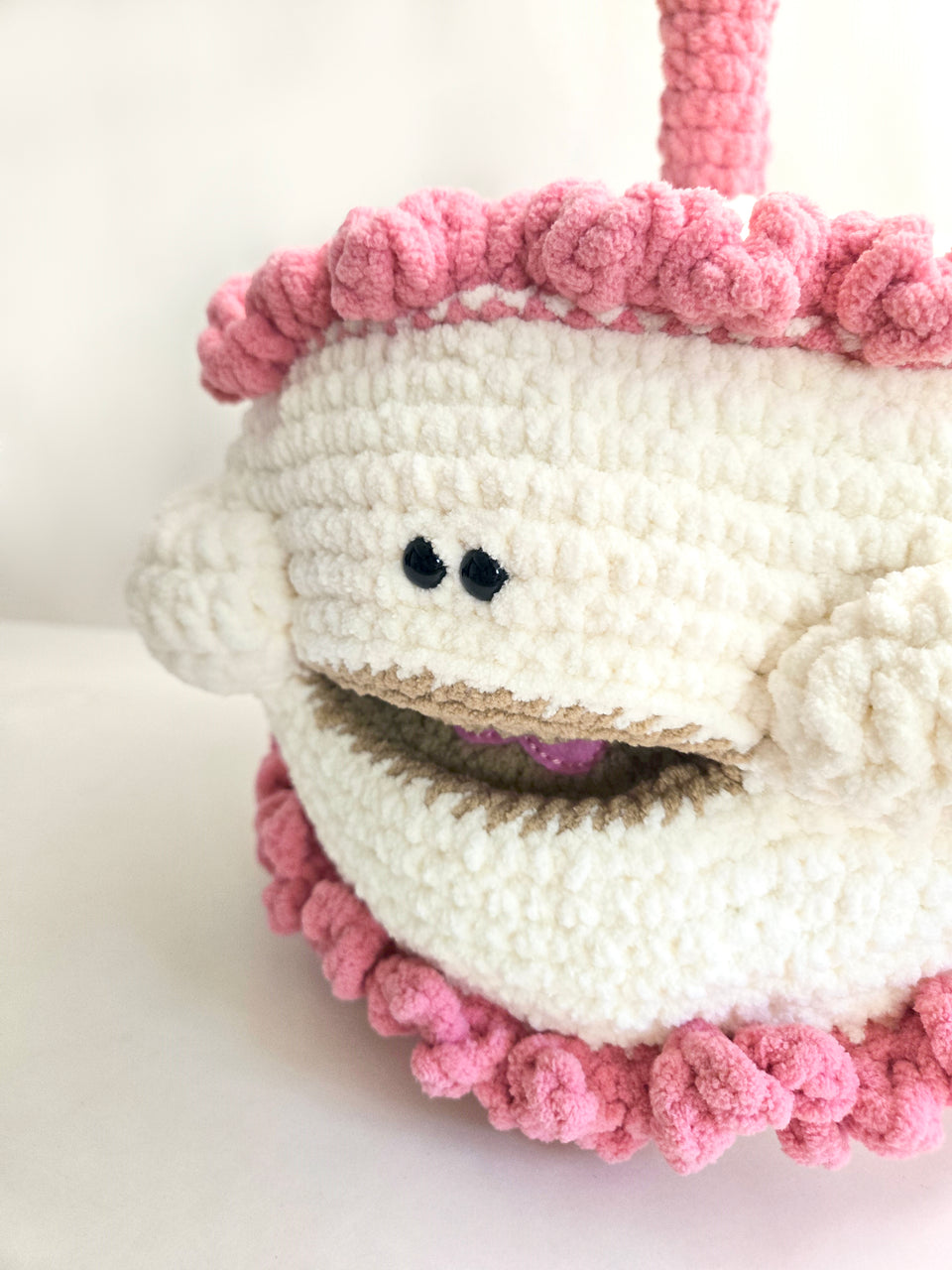 Close-up of a smiling crochet cake with with pink and white frosting on a light background