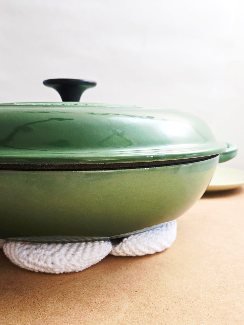 Green enameled cast iron skillet with lid on top for a crocheted flower trivet. 