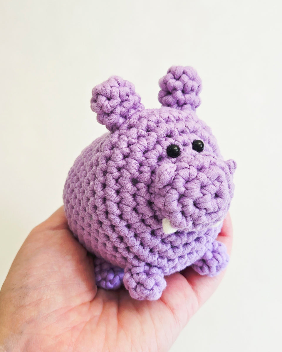 A small crocheted hippopotamus toy held in a person's hand against a plain light background.