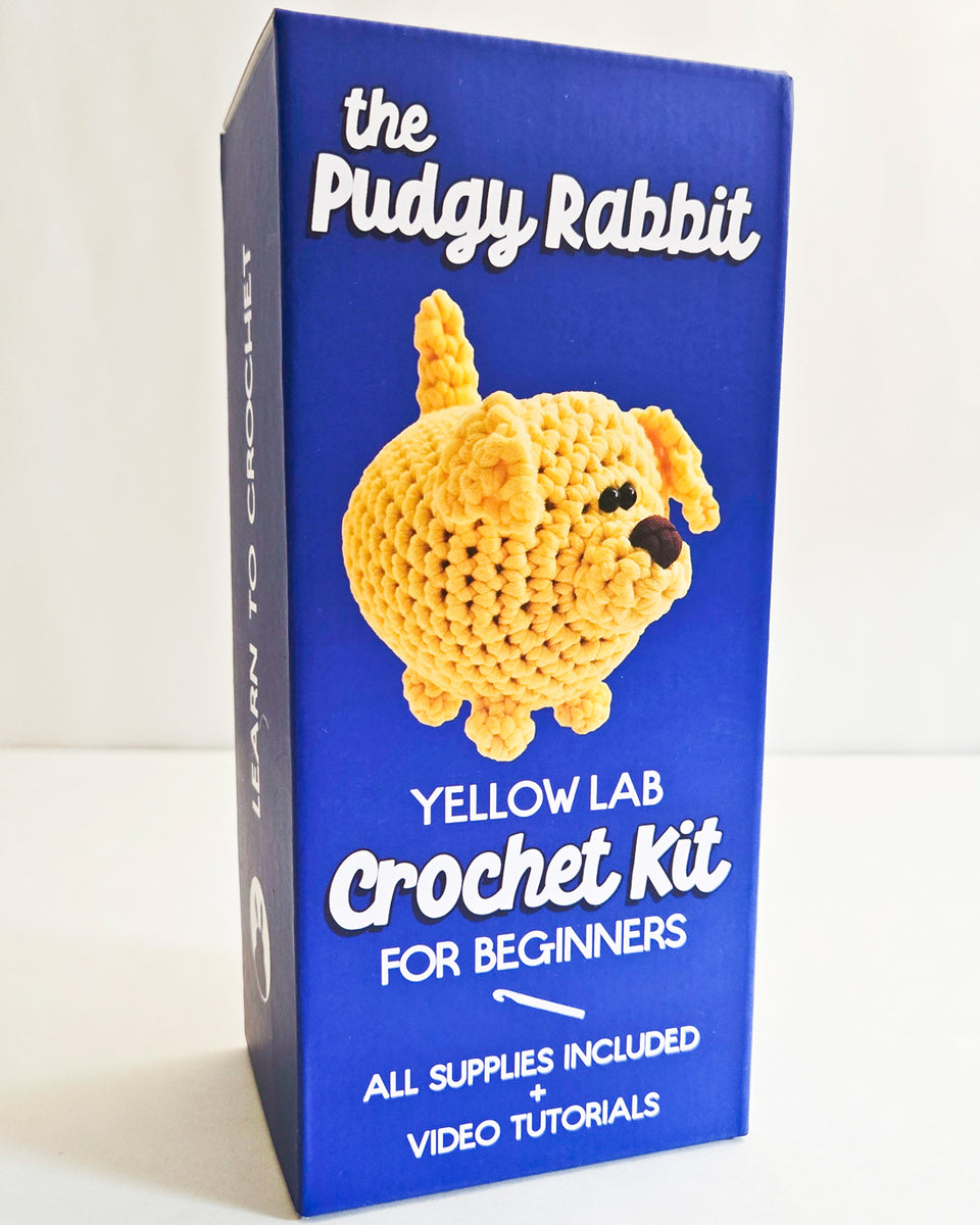 The Pudgy Rabbit Yellow Lab Crochet Kit box, a deep blue package featuring a picture of a yellow crochet dog and white text, set against a plain white background.