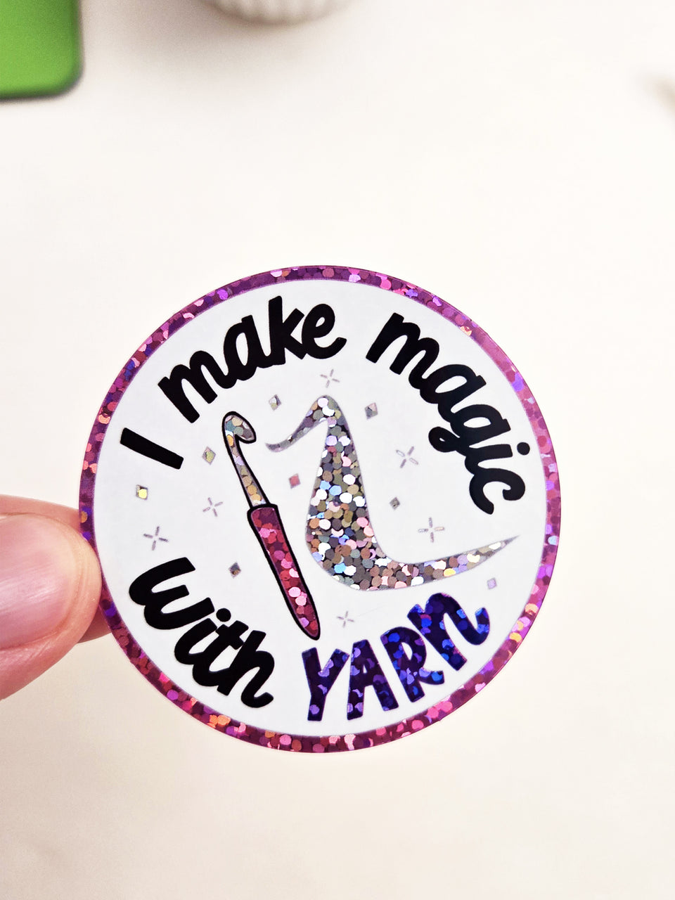 Round glitter sticker that says "I make magic with yarn" with a crochet hook in the middle.