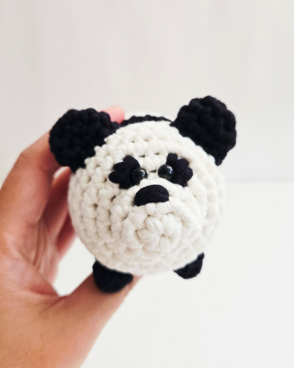 A hand holding a small crocheted panda toy against a plain white background. Panda from learn to crochet kit by The Pudgy Rabbit.