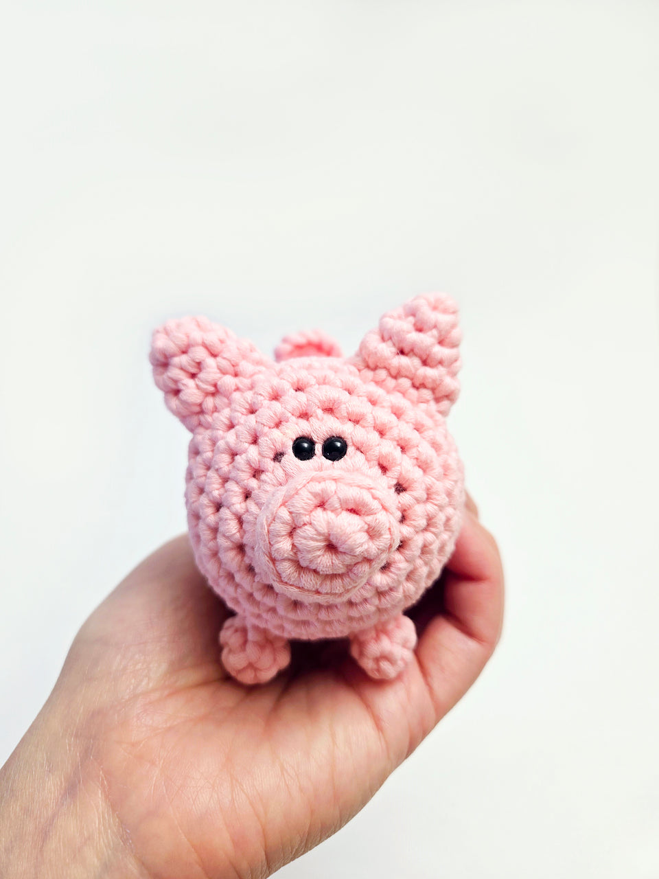 Mini crochet pig being held in the palm of a hand.