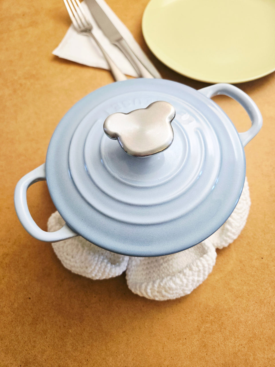 Light blue cast iron pot with a lid on top of a crocheted flower trivet.