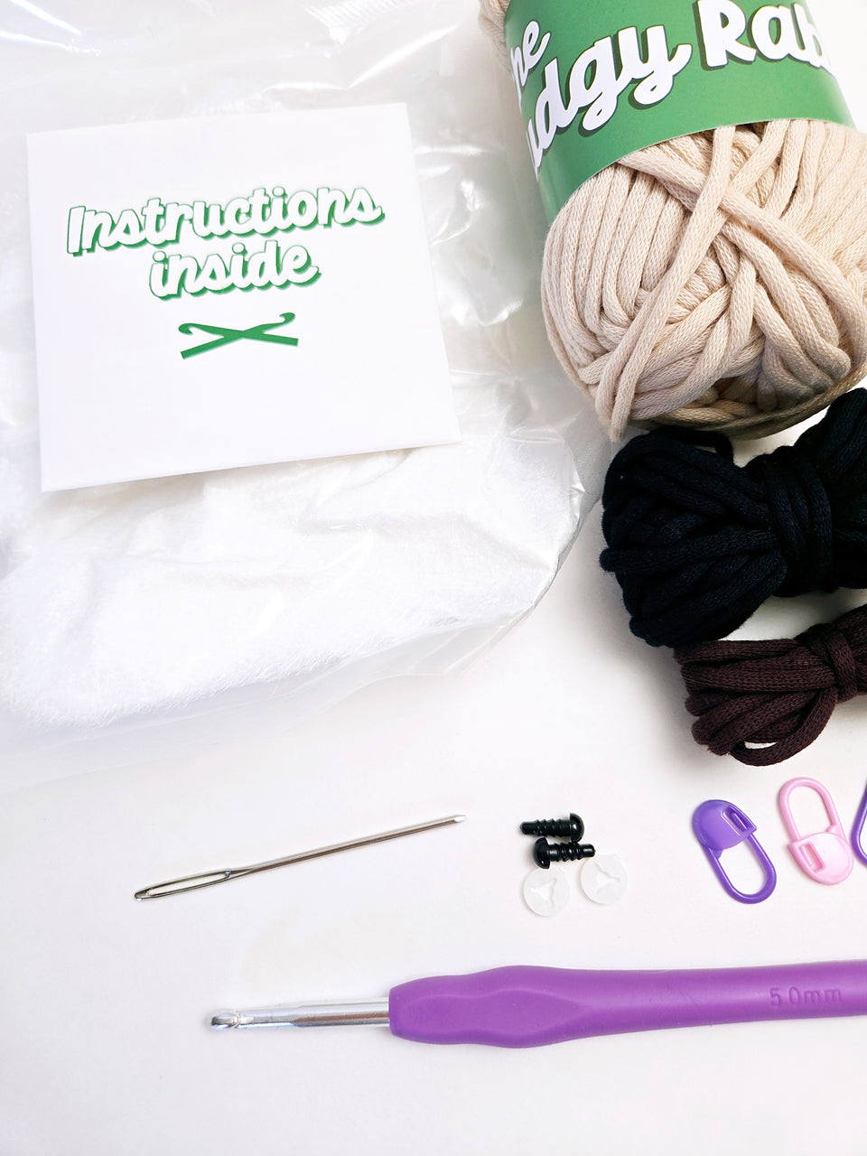 Close up of crochet kit supplies, including yarn, crochet hook, yarn needle, safety eyes, stitch markers, stuffing, and instruction packet.