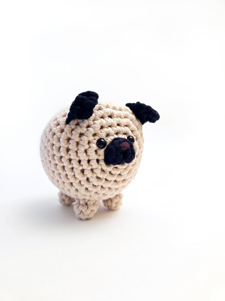 Light beige crochet pug amigurumi with black ears and muzzle.