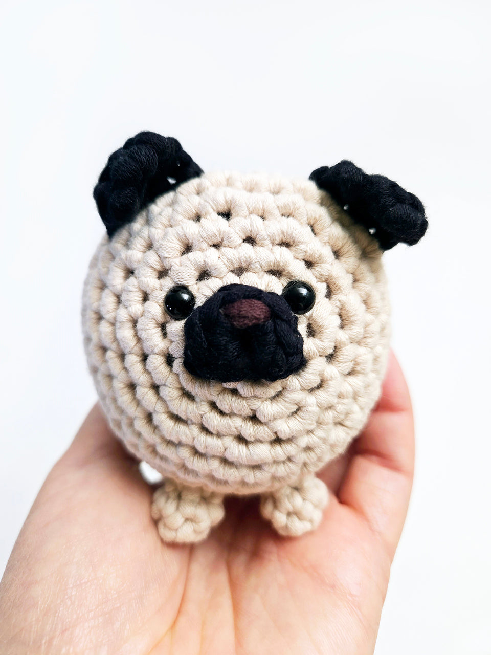 Black and tan crochet pug being held in a hand with a white background